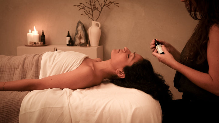 woman lies on bed with candles and face oils, dries flowers and crystals in massage